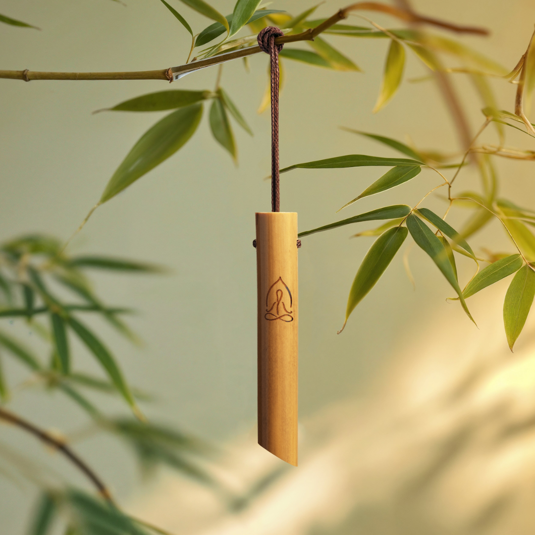The Mindful Bamboo Breathing Necklace hanging on a black cord in front of bamboo leaves