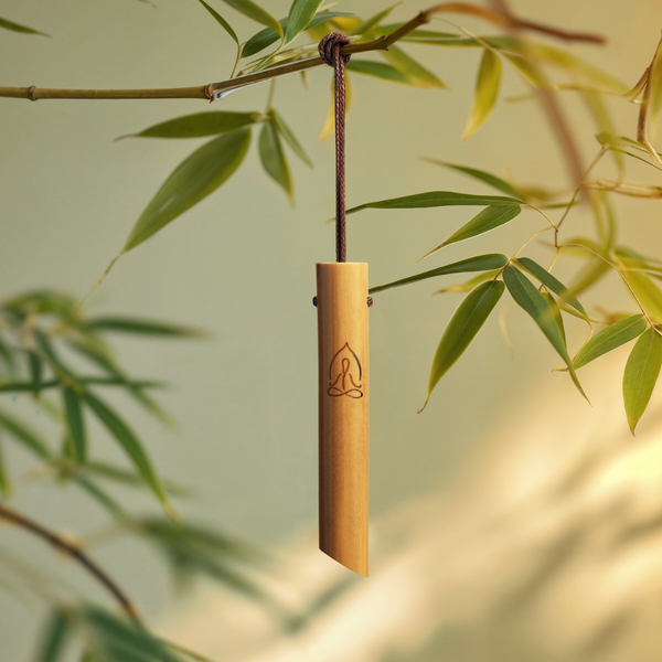 The Mindful Bamboo Breathing Necklace hanging on a black cord in front of bamboo leaves