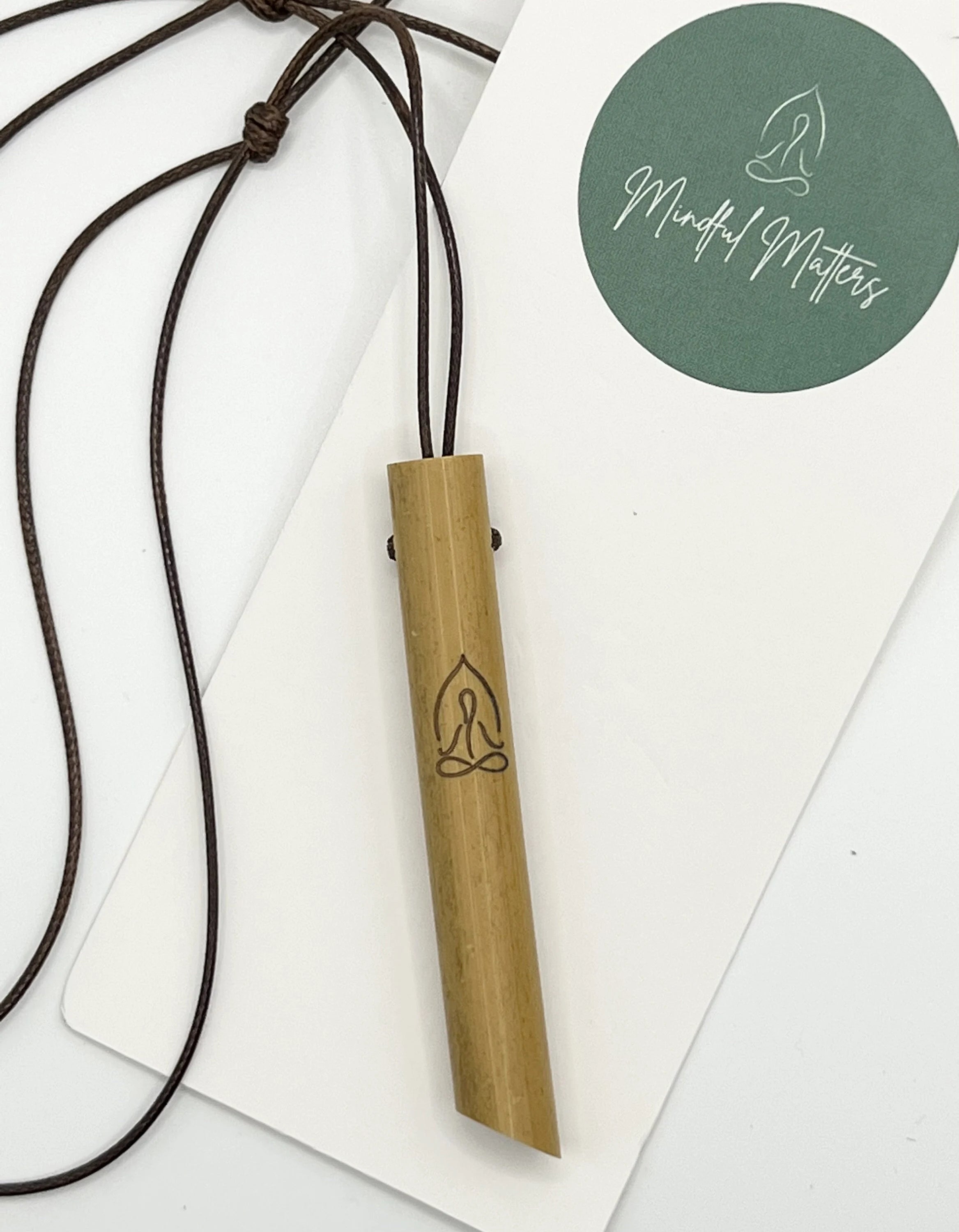 The Mindful Bamboo Breathing Necklace laid flat on a white surface with the brand's logo tag