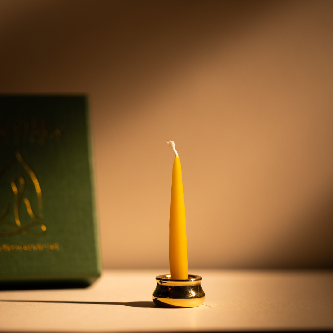 A lit beeswax candle in the brass holder beside the dark green Mindful Matters box